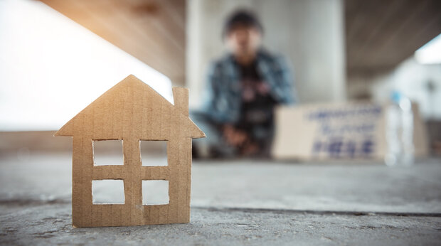 Dakloze onder een viaduct, op de voorgrond staat een huisje geknipt uitkarton