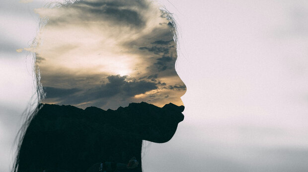 Silhouette van een vrouw, in het silhouette is een bewolkte lucht te zien