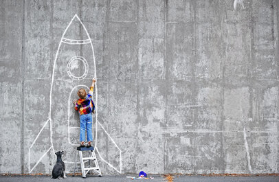 Jongetje tekent met krijt een grote raket op een muur