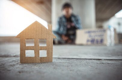Dakloze onder een viaduct, op de voorgrond staat een huisje geknipt uitkarton