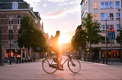 Man op fiets in binnenstad Leuven. Aan het eind van de straat komt de zon op.