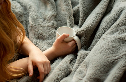 Vrouw onder een deken met een beker thee