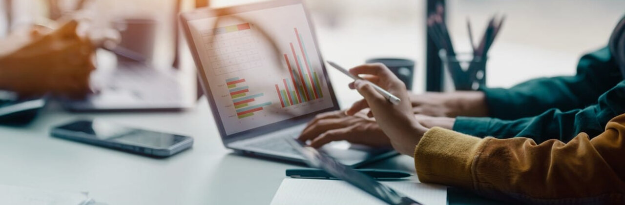 Twee personen wijzen naar een scherm waarop grafieken te zien zijn.