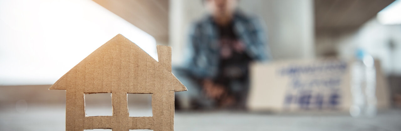 Dakloze onder een viaduct, op de voorgrond staat een huisje geknipt uitkarton