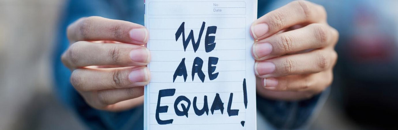 Iemand houdt papier omhoog met de tekst 'we are equal'
