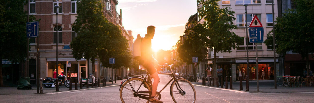 Man op fiets in binnenstad Leuven. Aan het eind van de straat komt de zon op.