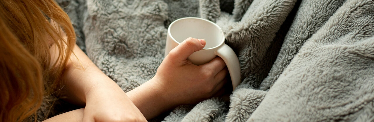 Vrouw onder een deken met een beker thee