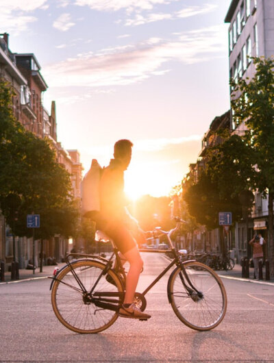 Man op fiets in binnenstad Leuven. Aan het eind van de straat komt de zon op.