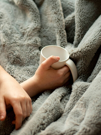 Vrouw onder een deken met een beker thee